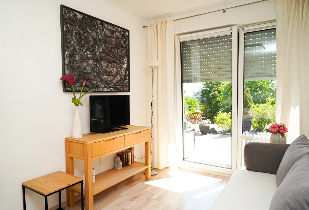 Wohn- oder Schlafbereich der Ferienwohnung mit Smart-TV und großen Fenstertüren, die direkt auf die eigene Terrasse führen.