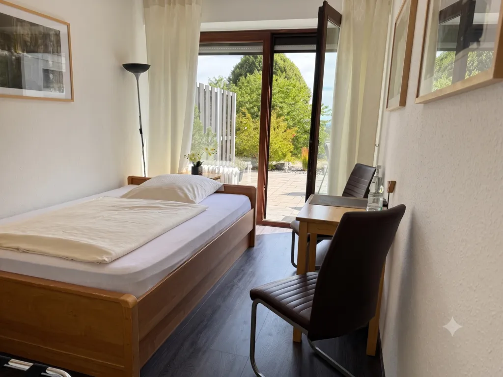 Ruhiges Einzelzimmer mit Sitzgelegenheit und direkter Tür zur sonnigen Terrasse und zum Garten.